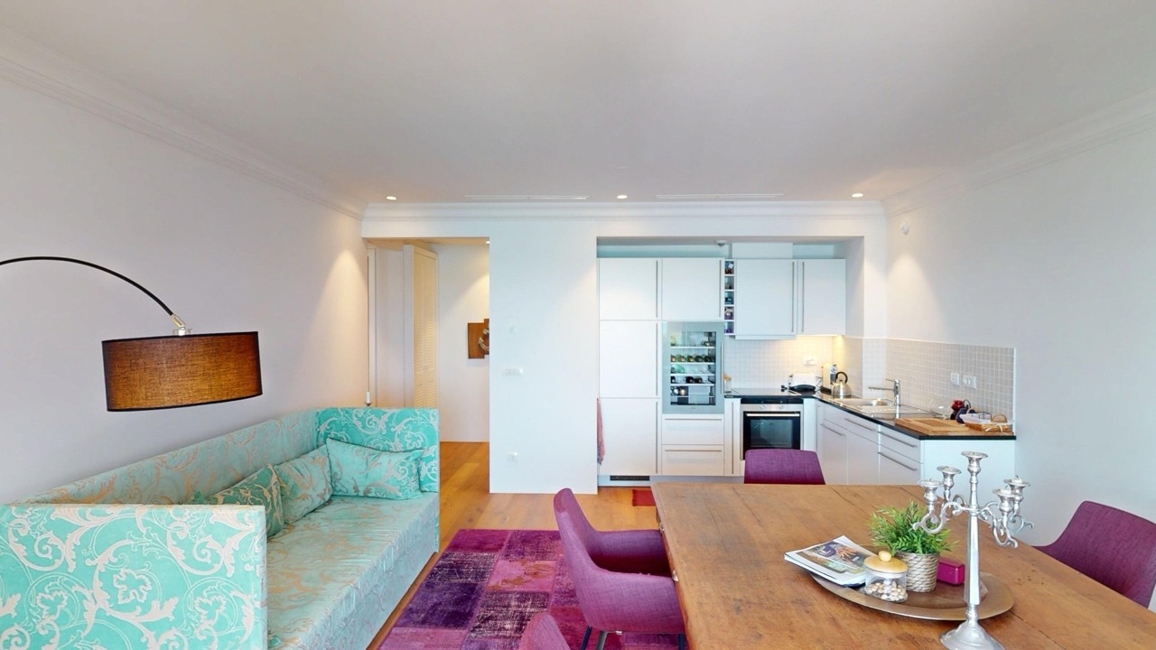 Wohnzimmer mit Küche in der Wohnung Luštica Bay, Radovići, Montenegro: türkisfarbenes Sofa, Esstisch und moderne Küche.