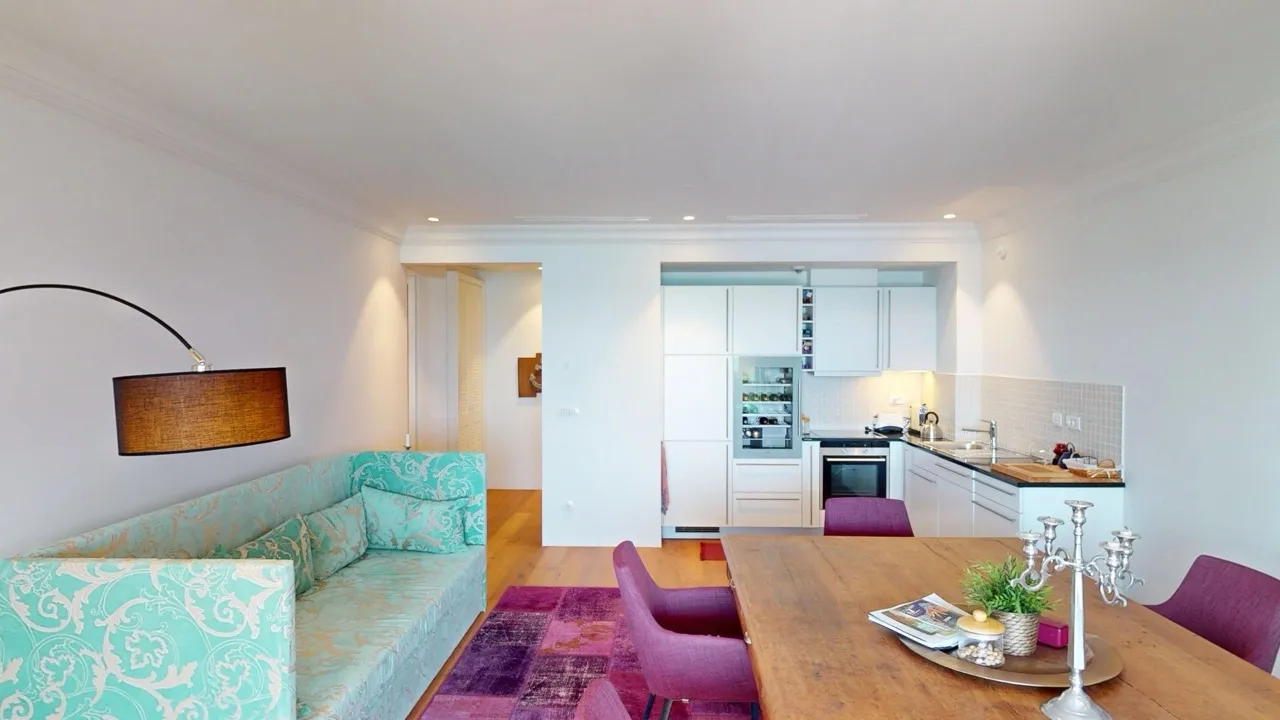 Dnevna soba sa kuhinjom u stanu Luštica Bay, Radovići, Crna Gora: tirkizna sofa, trpezarijski sto i moderna kuhinja.