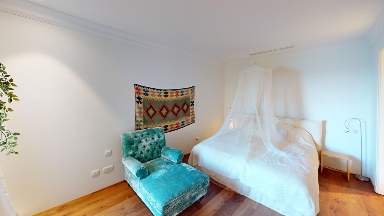 Schlafzimmer in der Wohnung in Luštica Bay, Radovići, Montenegro: Himmelbett, türkisfarbener Sessel und Wanddekoration.