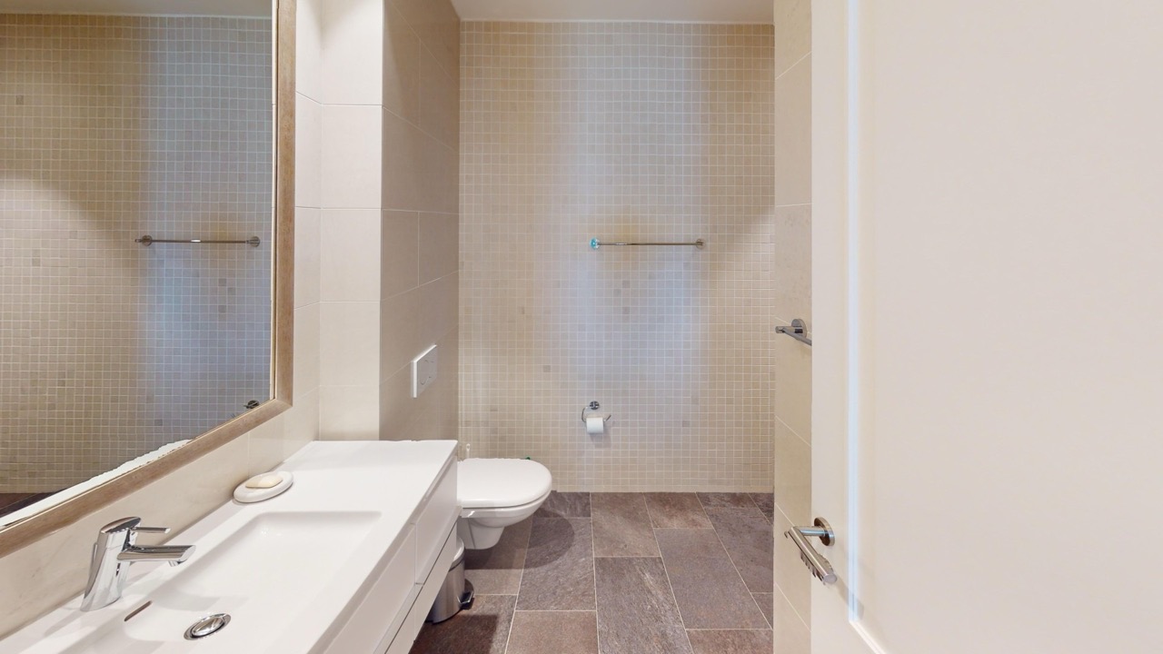 Modernes Badezimmer in der Wohnung in Luštica Bay, Radovići, Montenegro: helle Fliesen, Spiegel und Sanitäranlagen.