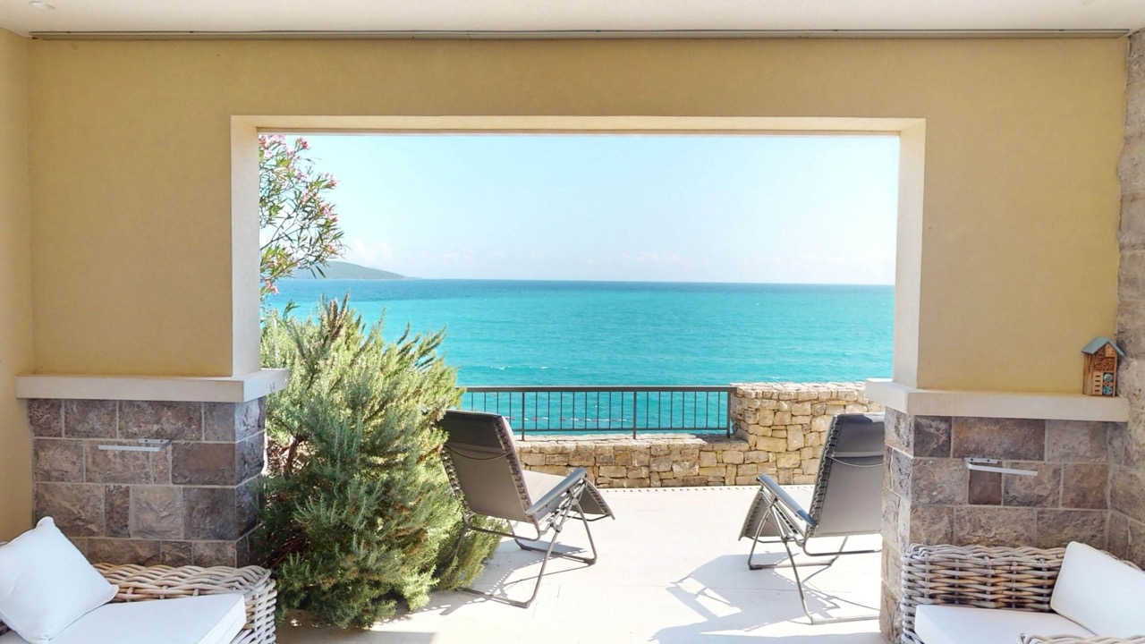 Terrasse mit Meerblick in den Apartments von Luštica Bay, Radovići, Montenegro: Rattanmöbel und Liegestühle an der Küste.