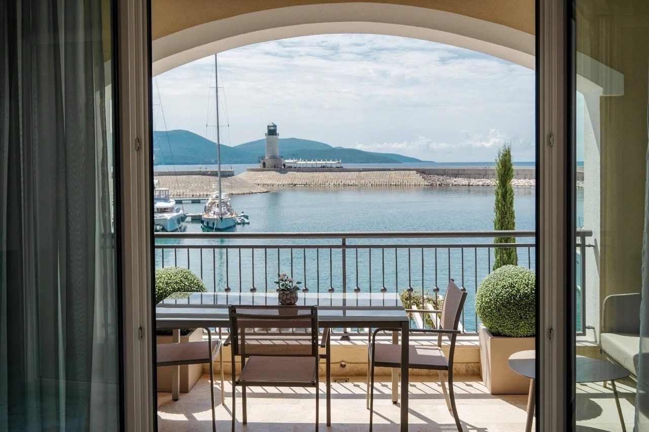 Blick vom Balkon der Wohnung in Luštica Bay, Radovići, Montenegro: Essbereich, Yachthafen und Leuchtturm vor dem Meer.