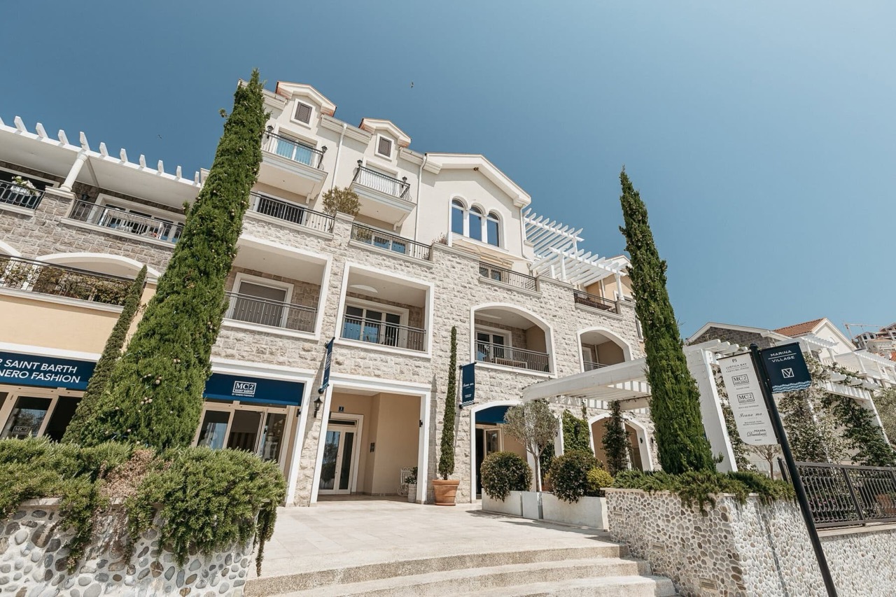 Fassade des Wohnkomplexes Lustica Bay in Radovici, Montenegro: Steinverkleidung, Balkone und Geschäfte im Erdgeschoss.