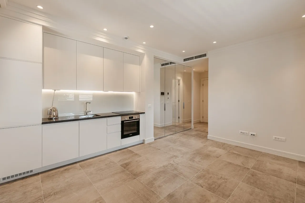 Moderne Küche in der Wohnung in Luštica Bay, Radovići, Montenegro: weiße Fronten, Einbaugeräte und ein Spiegelschrank.