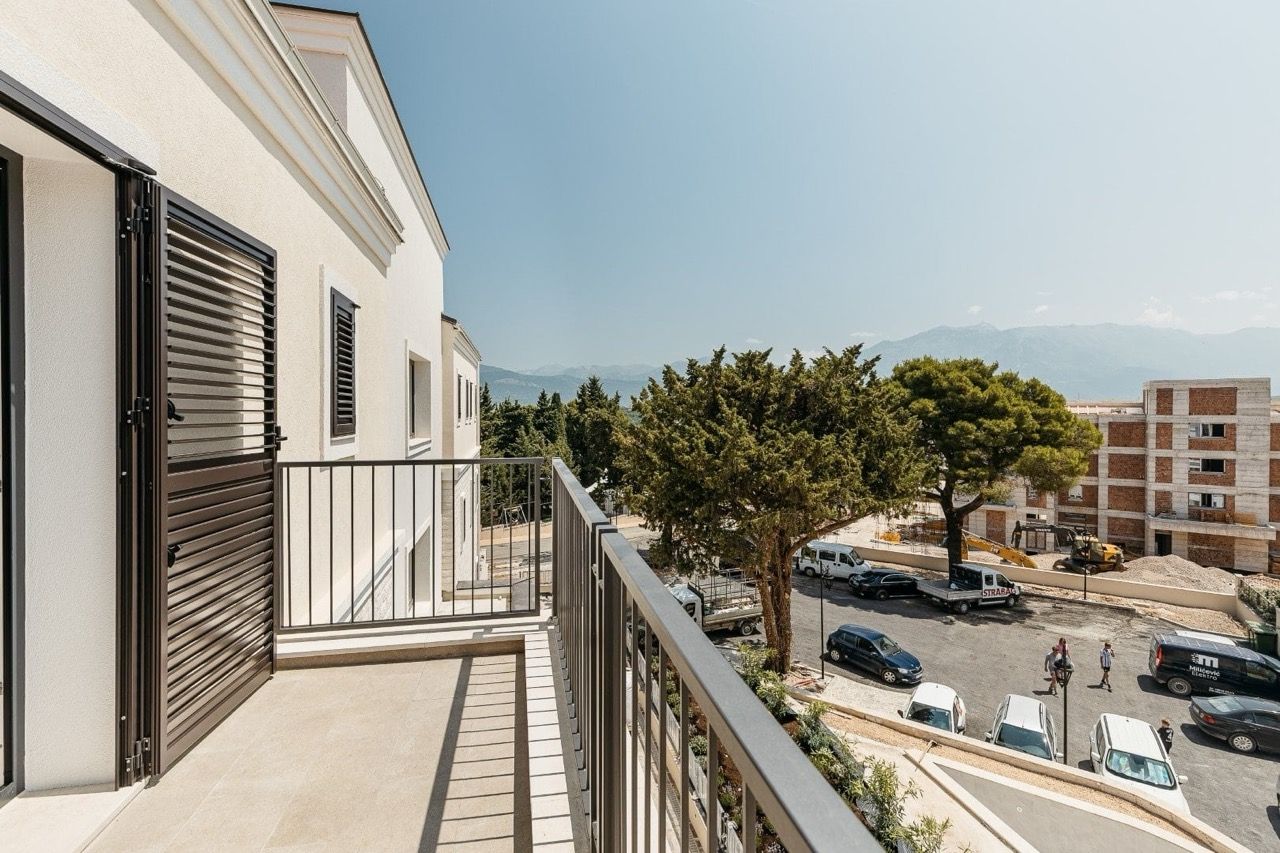 Balcon d’un appartement moderne à Luštica Bay, Radovići, Monténégro, avec vue sur les montagnes et le parking du complexe résidentiel.