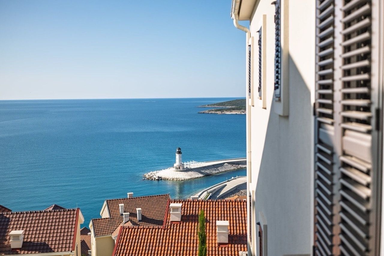 Vue depuis la fenêtre de l’appartement à Luštica Bay, Radovići, Monténégro : mer, phare et toits en tuiles des maisons sur le littoral.
