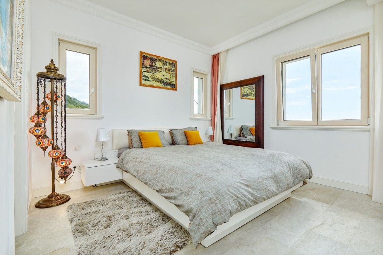Chambre lumineuse dans l’appartement Luštica Bay, Radovići, Monténégro : lit double, lampadaire oriental et vue depuis les fenêtres.