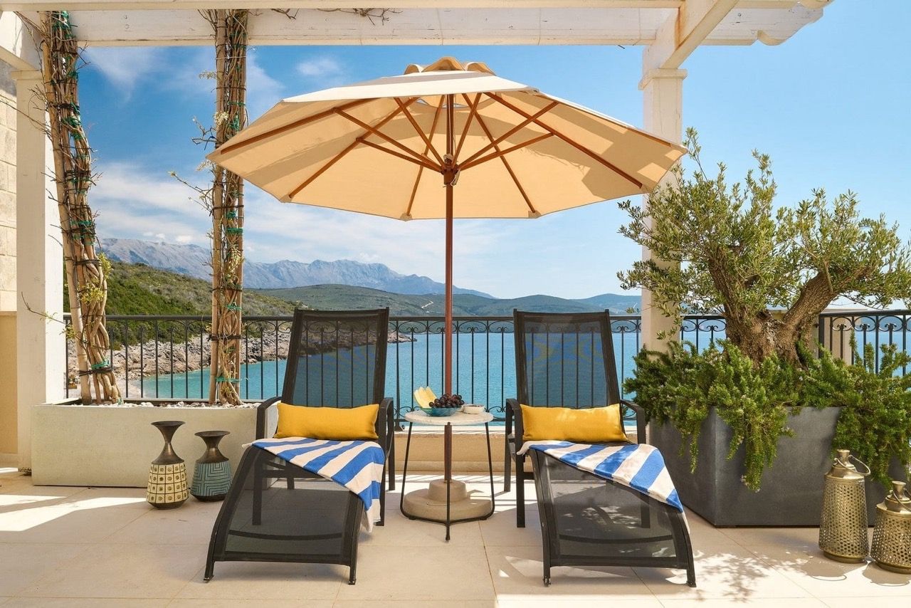 Terrasse avec chaises longues et parasol à Luštica Bay, Radovići, Monténégro : vue sur la mer et les montagnes, mobilier élégant pour se détendre.
