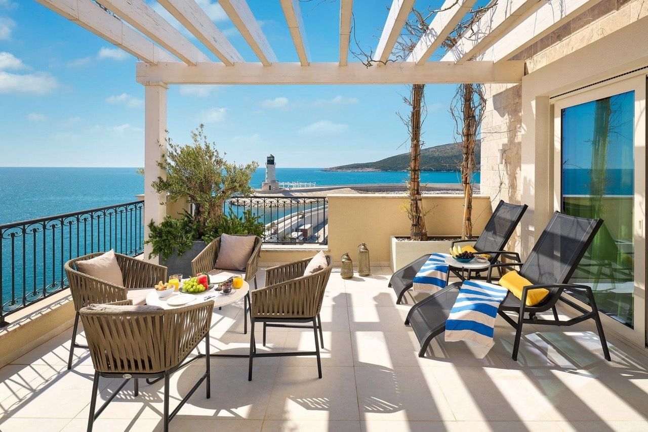 Terrasse de l’appartement à Luštica Bay, Radovići, Monténégro : vue sur la mer, phare, mobilier en osier et chaises longues sous une pergola.