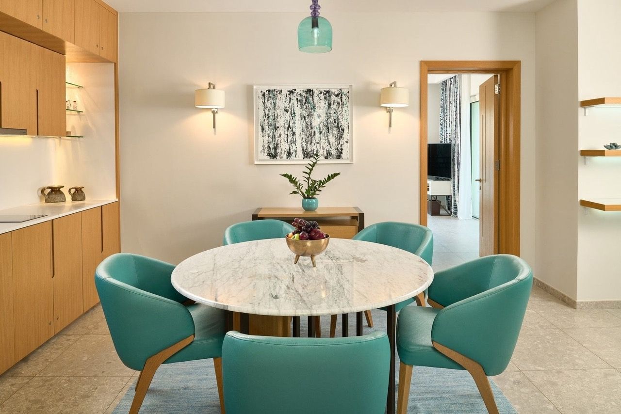 Coin repas avec table en marbre et fauteuils turquoise dans l’appartement Lustica Bay, Radovići, Monténégro.