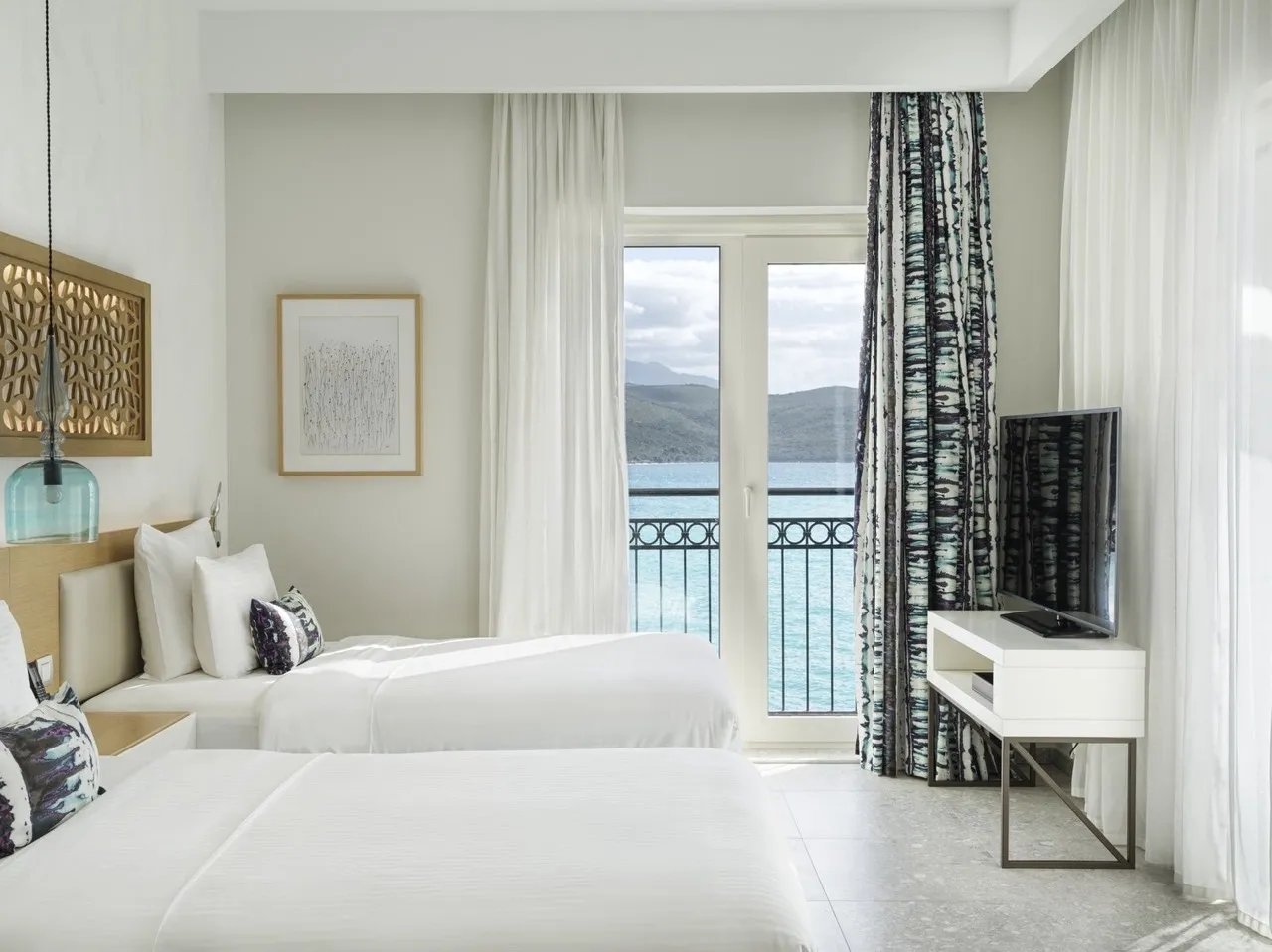 Спальня в апартаментах Lustica Bay, Радовичи, Черногория: две кровати, современная мебель и вид на море с балкона.