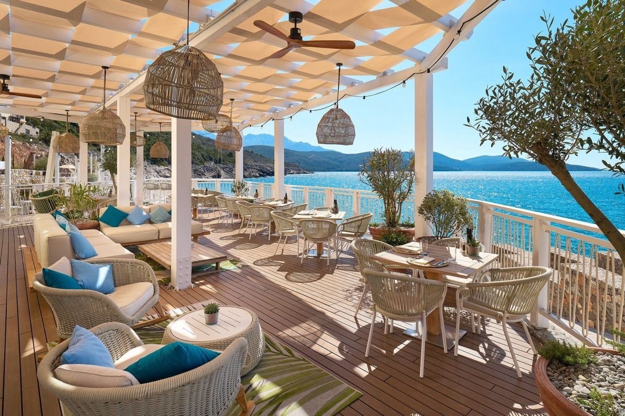 Terrasse du restaurant à Luštica Bay, Radovići, Monténégro : mobilier en osier, auvent, vue sur la mer et les montagnes.