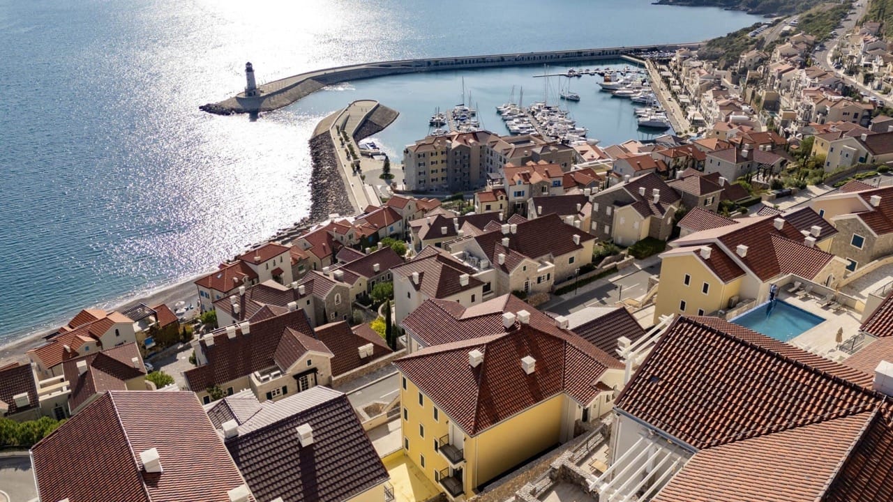 Panoramic view of the Lustica Bay residential complex in Radovici, Montenegro: villas with tiled roofs, a pool, and a marina.