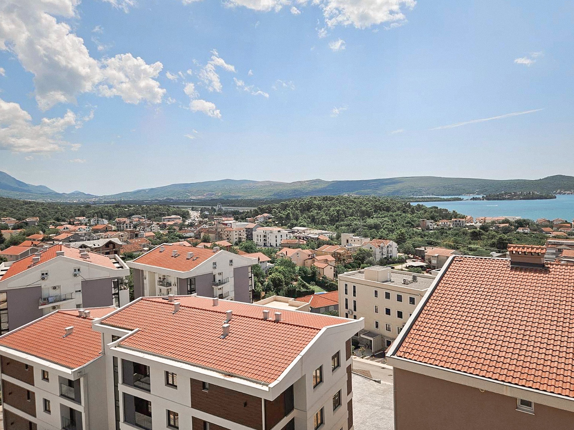 Panoramiczny widok na Tivat i Morze Adriatyckie z okien mieszkania w Czarnogórze, nowoczesne domy z czerwoną dachówką.