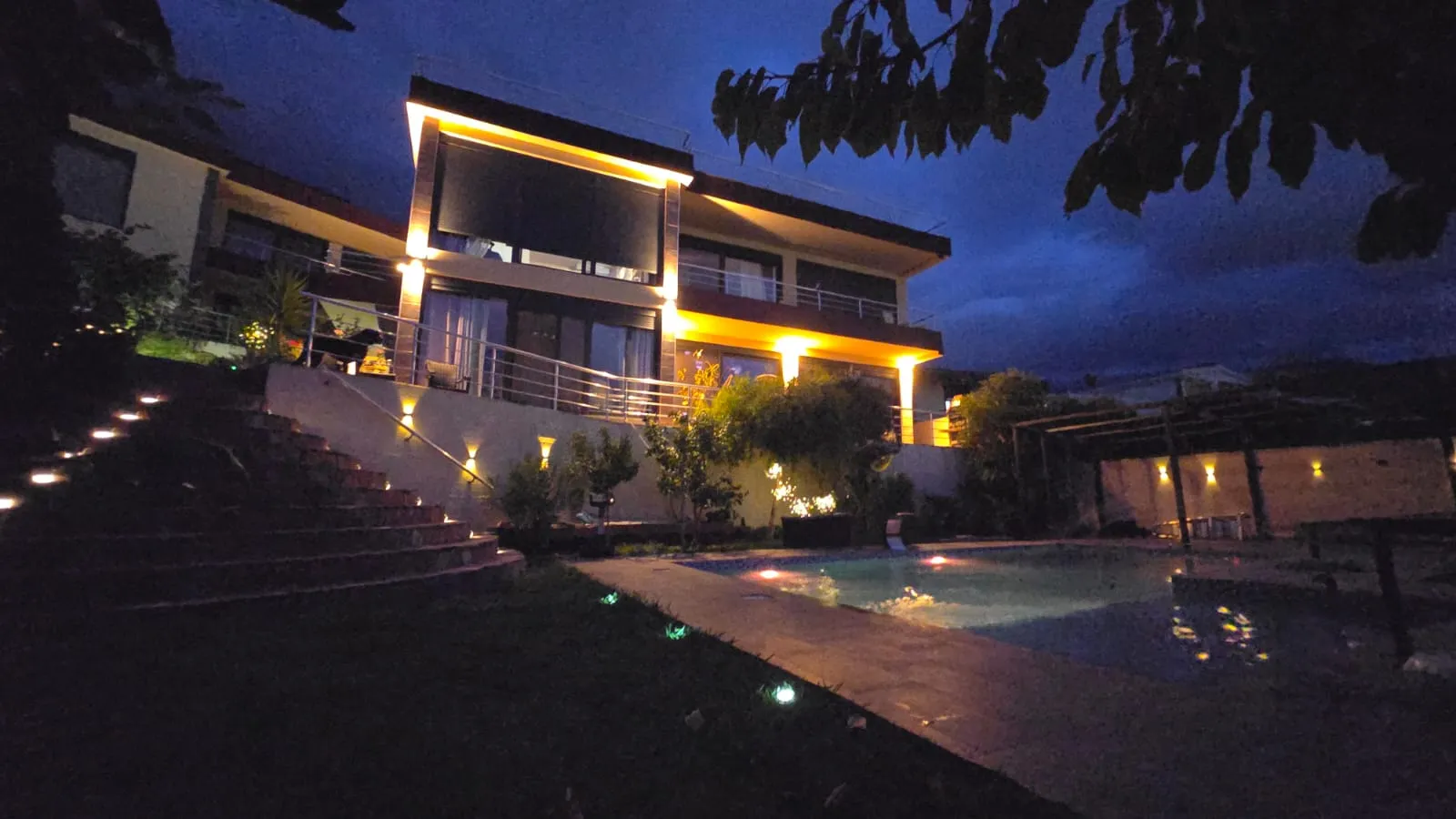 Moderne Villa in Bar, Montenegro: nächtliche Fassadenbeleuchtung, Terrasse, Treppe und Außenpool im Hof.