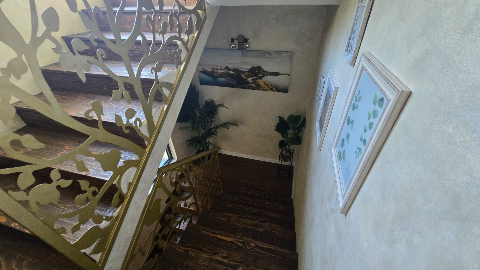 Drewniane schody z ażurową balustradą we wnętrzu willi w mieście Bar, Czarnogóra, z dekoracjami i obrazami na ścianach.