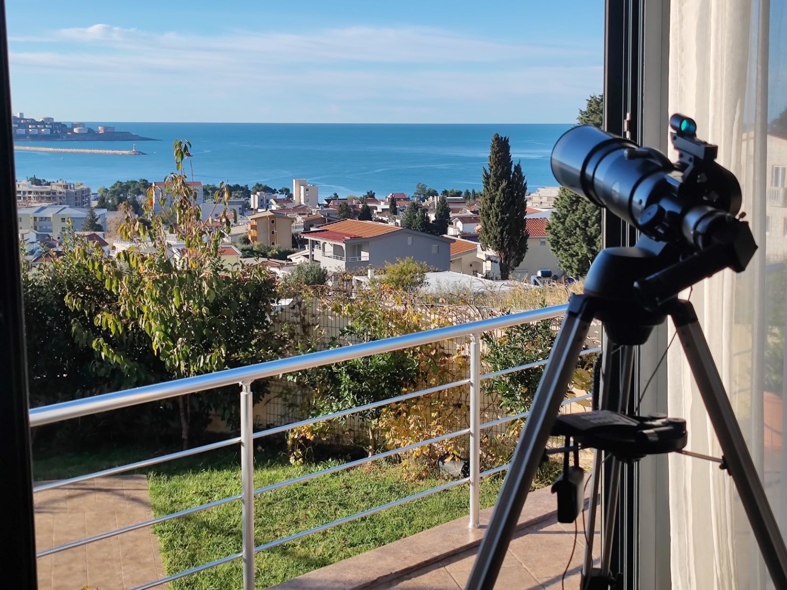 Widok z balkonu willi w Barze, Czarnogóra: panorama morza i miasta, teleskop na statywie, taras z balustradą.
