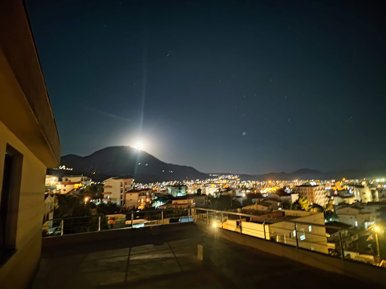 Nocny widok z tarasu willi w mieście Bar, Czarnogóra: panorama miasta, światła domów i góry pod księżycowym niebem.