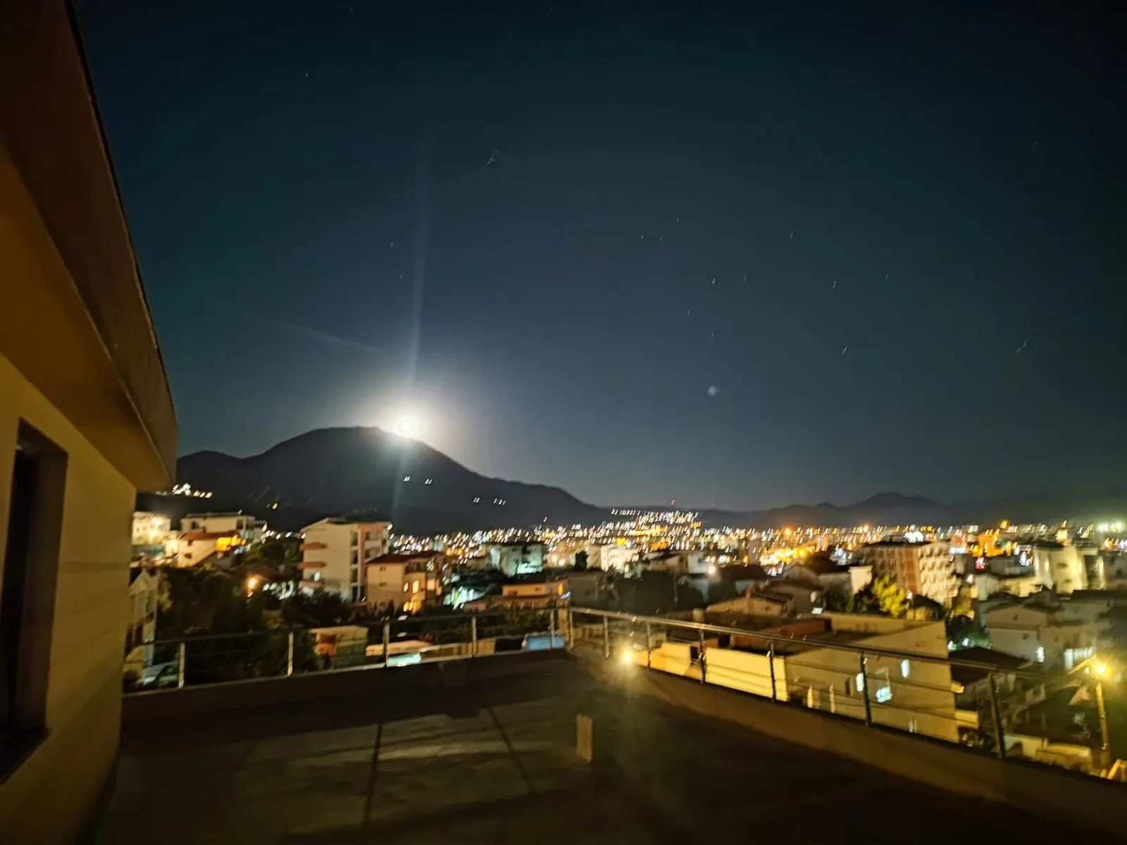 Nachtansicht von der Terrasse einer Villa in der Stadt Bar, Montenegro: Panorama der Stadt, Lichter der Häuser und Berge unter dem Mondhimmel.