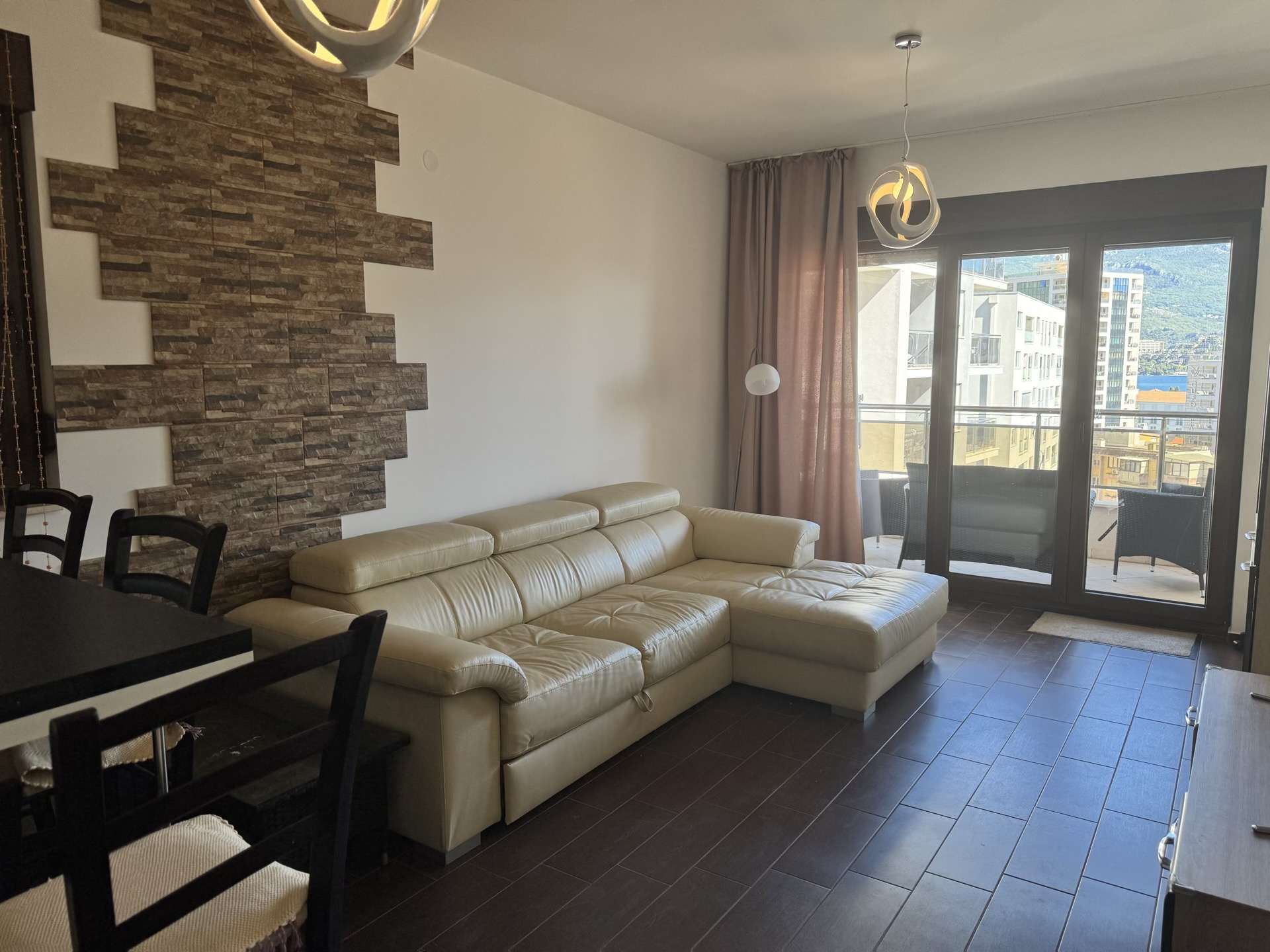 Living room in an apartment in Budva, Montenegro: leather sofa, stone accent wall, and access to a terrace with city views.