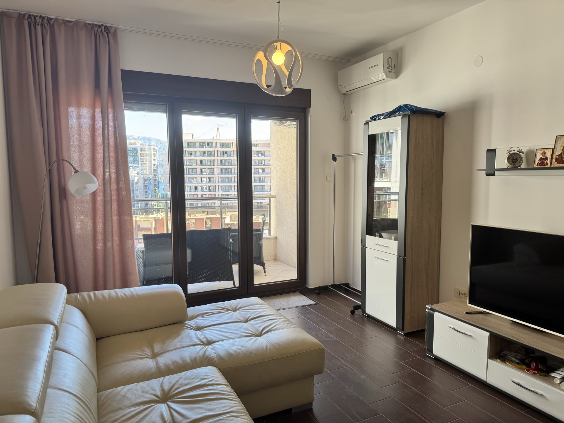 Living room in an apartment in Budva, Montenegro: a light sofa, modern furniture, and access to a terrace with city views.