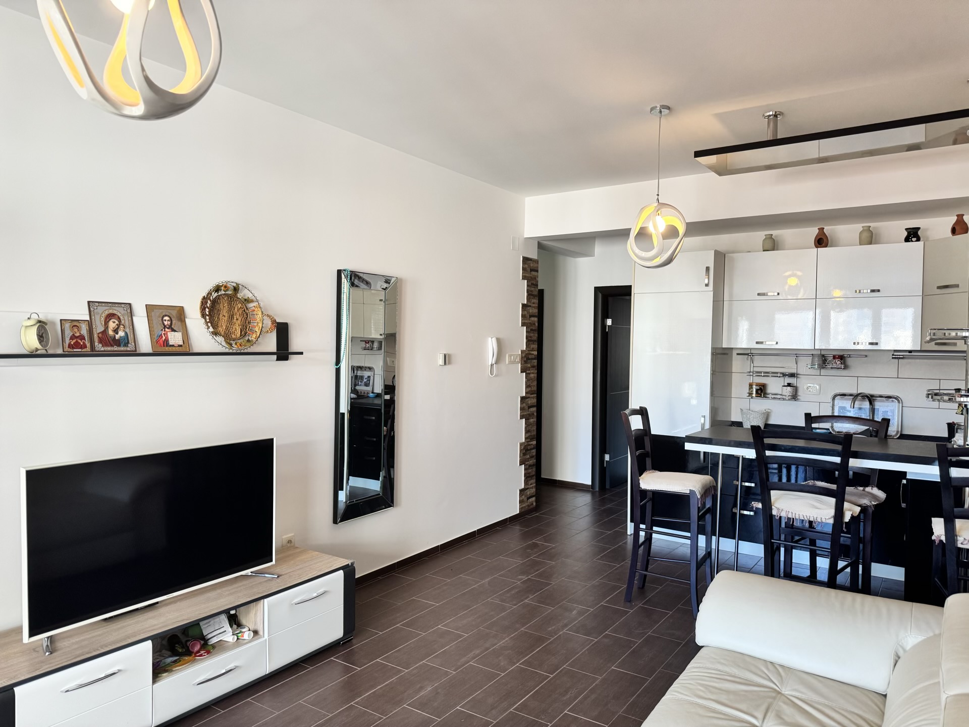 Modern living room with kitchen in an apartment in Budva, Montenegro: white furniture, a bar counter, and a TV area.