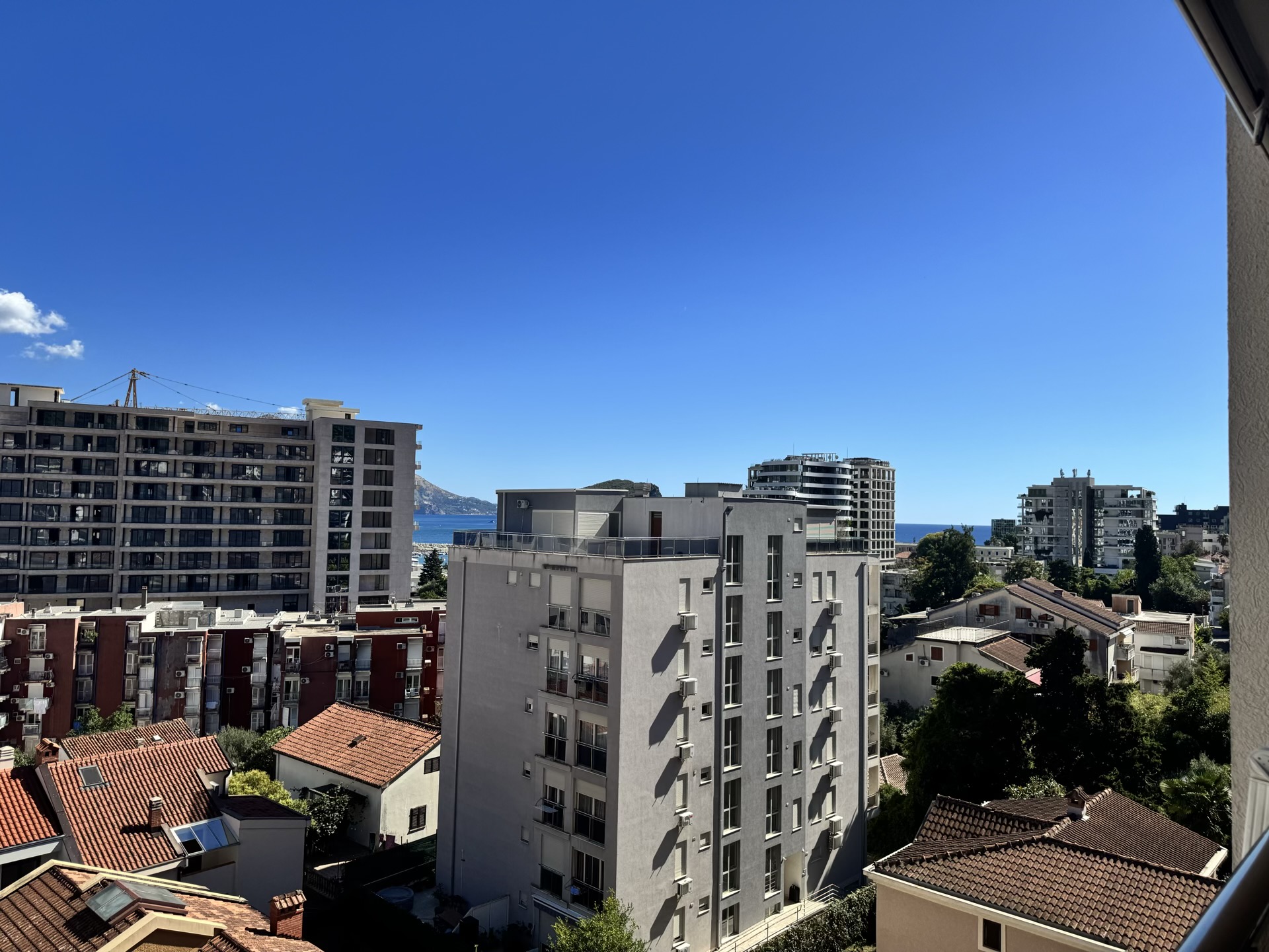 View from the apartment window in Budva, Montenegro: a city panorama with modern residential buildings and the sea horizon.