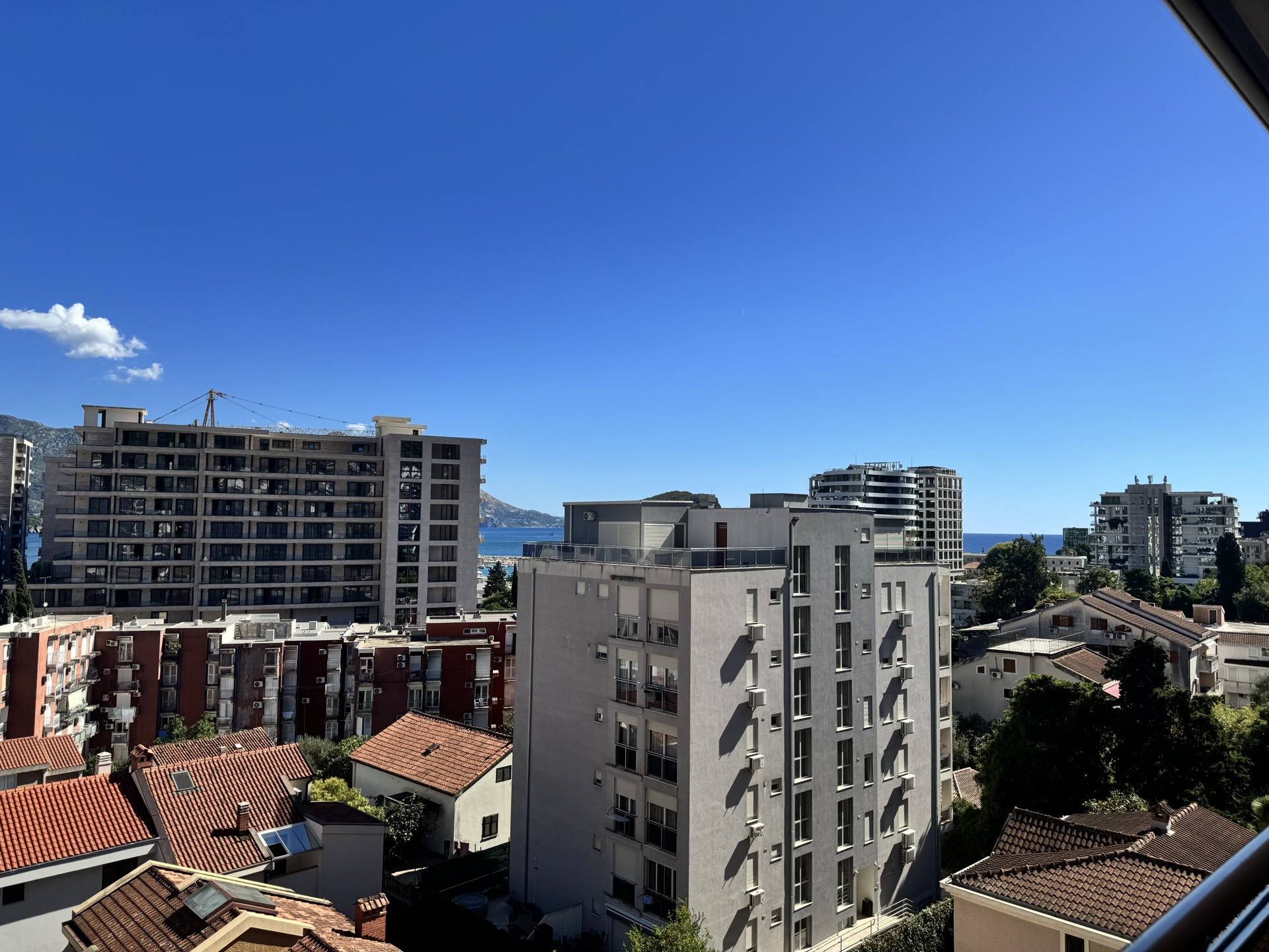 View from the apartment balcony in Budva, Montenegro: a panorama of the city with modern buildings and the sea horizon.