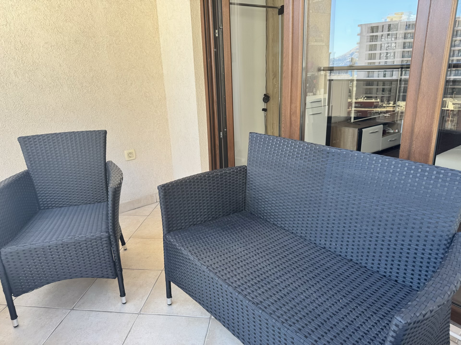 Terrace with wicker furniture in an apartment in Budva, Montenegro: city view and panoramic balcony glazing.