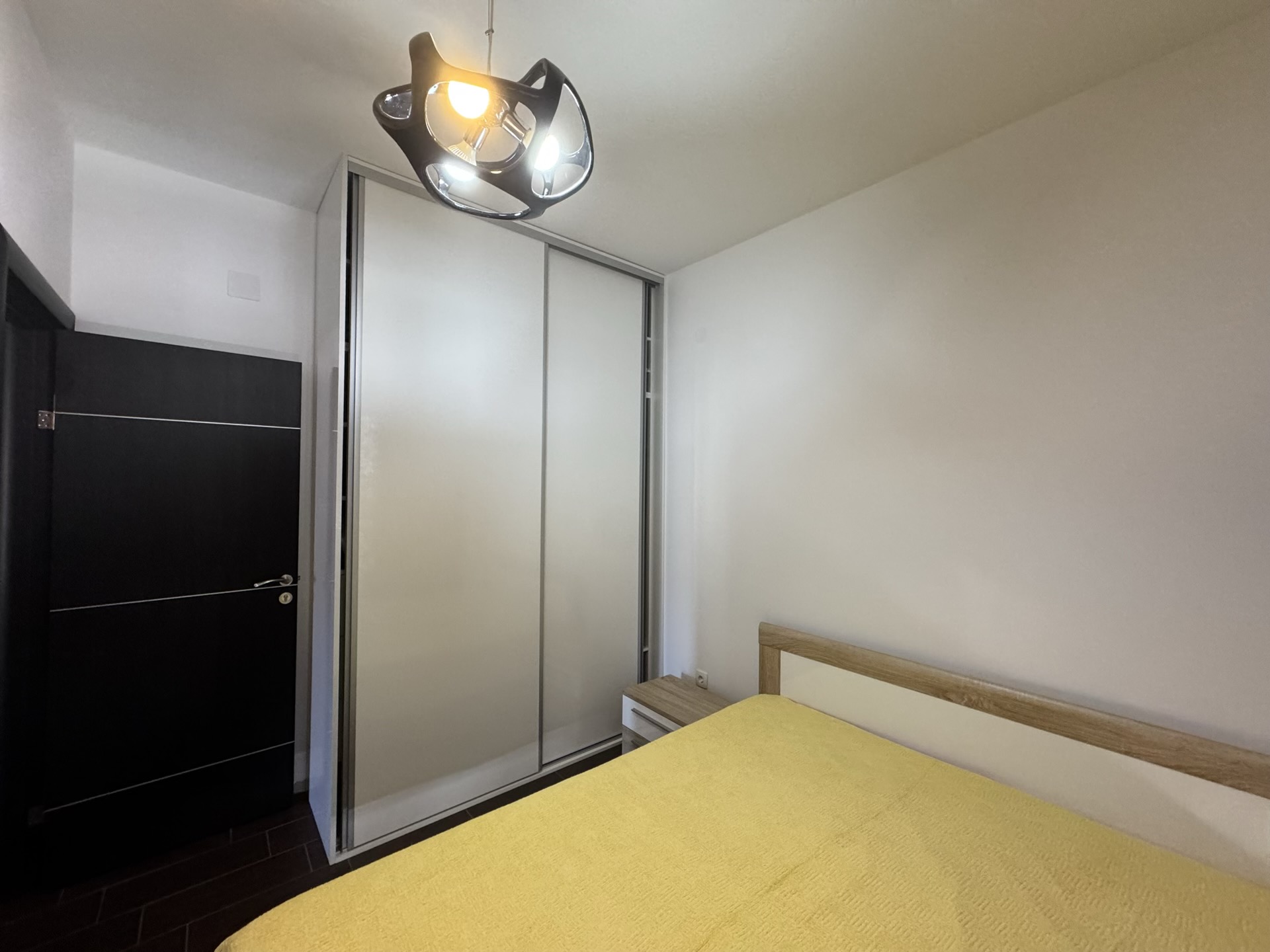 Bedroom in an apartment in Budva, Montenegro: a double bed, built-in wardrobe, and a modern chandelier.
