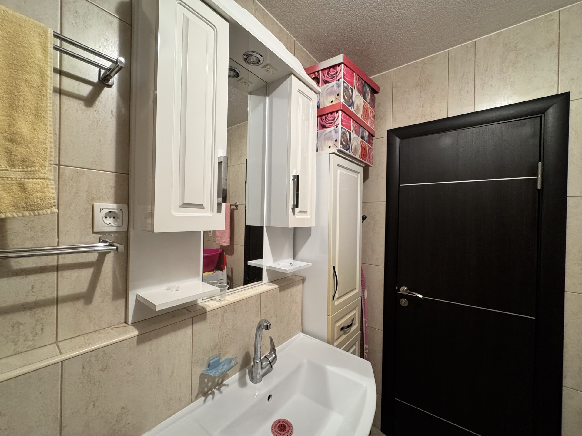 Bathroom in an apartment in Budva, Montenegro: white vanity with mirror, sink, and a dark interior door.
