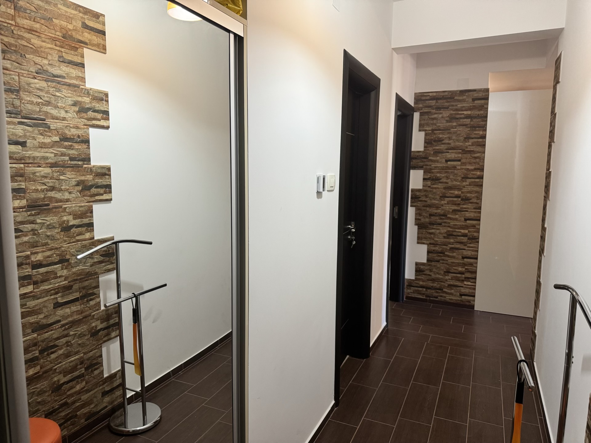 Modern hallway in an apartment in Budva, Montenegro: decorative stone finish, mirrored wardrobe, and dark tile.