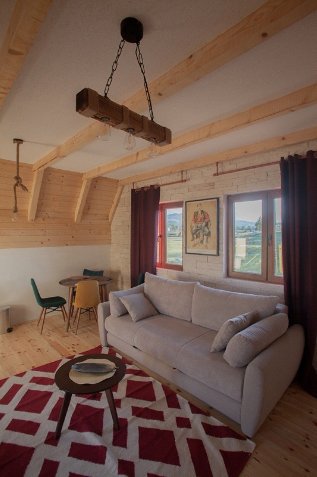 Rustic-style living room with wooden beams in a house, Žabljak, Montenegro: a light-colored sofa, dining area, and mountain view.