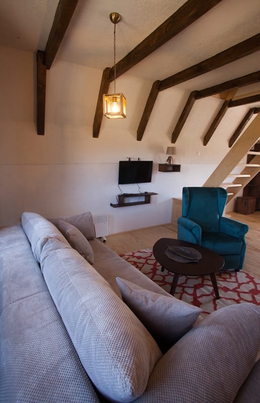 Living room in a house in Žabljak, Montenegro: attic with wooden beams, gray sofa, blue armchair, and staircase.