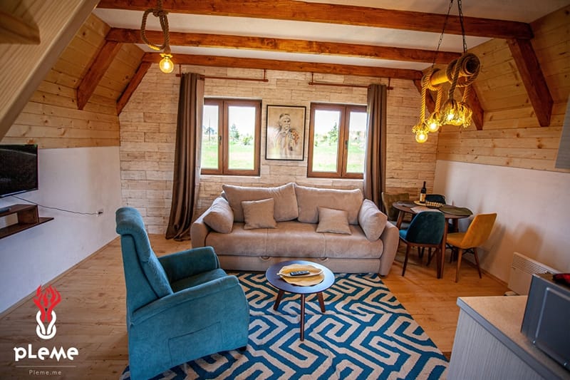 Cozy living room in a wooden house in Žabljak, Montenegro: a soft sofa, armchair, stone finishes, and a beamed ceiling.