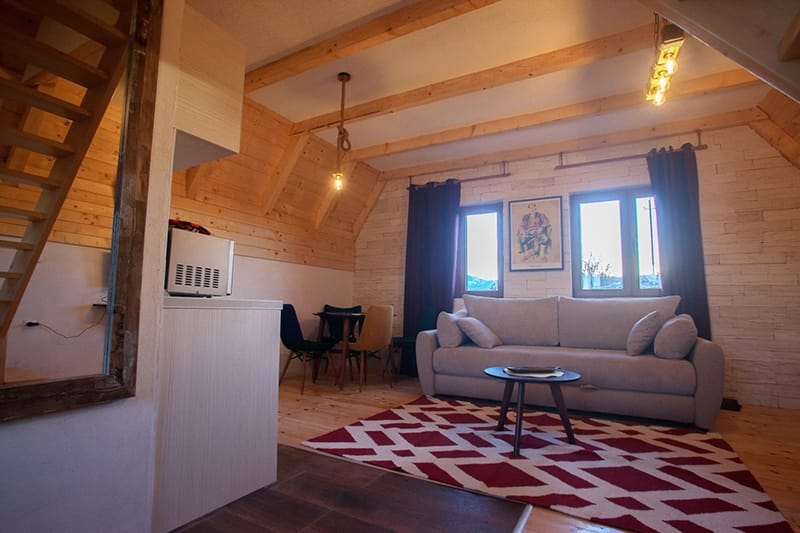 Living room in a wooden house in Žabljak, Montenegro: light-colored sofa, dining area, wood and stone finishes.