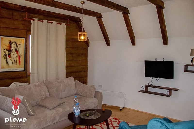 Salon w domu w Žabljaku, Czarnogóra: przytulne wnętrze z drewnianymi belkami, miękką sofą i strefą TV.
