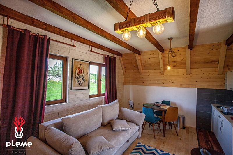 Rustic-style living room with wooden beams in a house, Žabljak, Montenegro: a soft sofa, dining area, and mountain view.