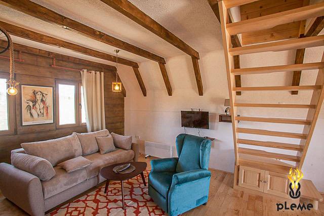 Living room in a wooden style with a staircase in the house, Žabljak, Montenegro: a soft sofa, armchair, and beamed ceiling.