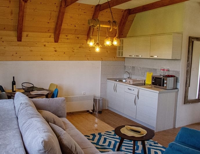 Living room with kitchen in a wooden house in Žabljak, Montenegro: light furniture, a sloped ceiling, and a stylish light fixture.