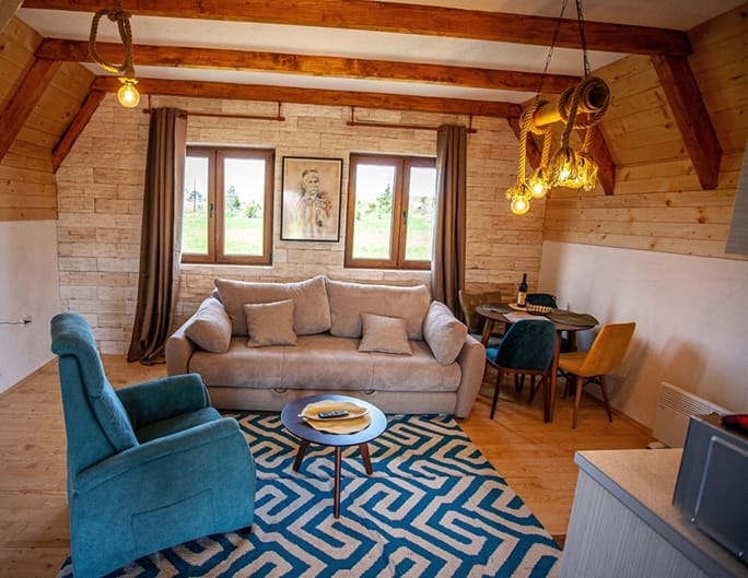 Living room in a wooden house in Žabljak, Montenegro: a cozy interior with rope pendant lights, a sofa, and mountain views.