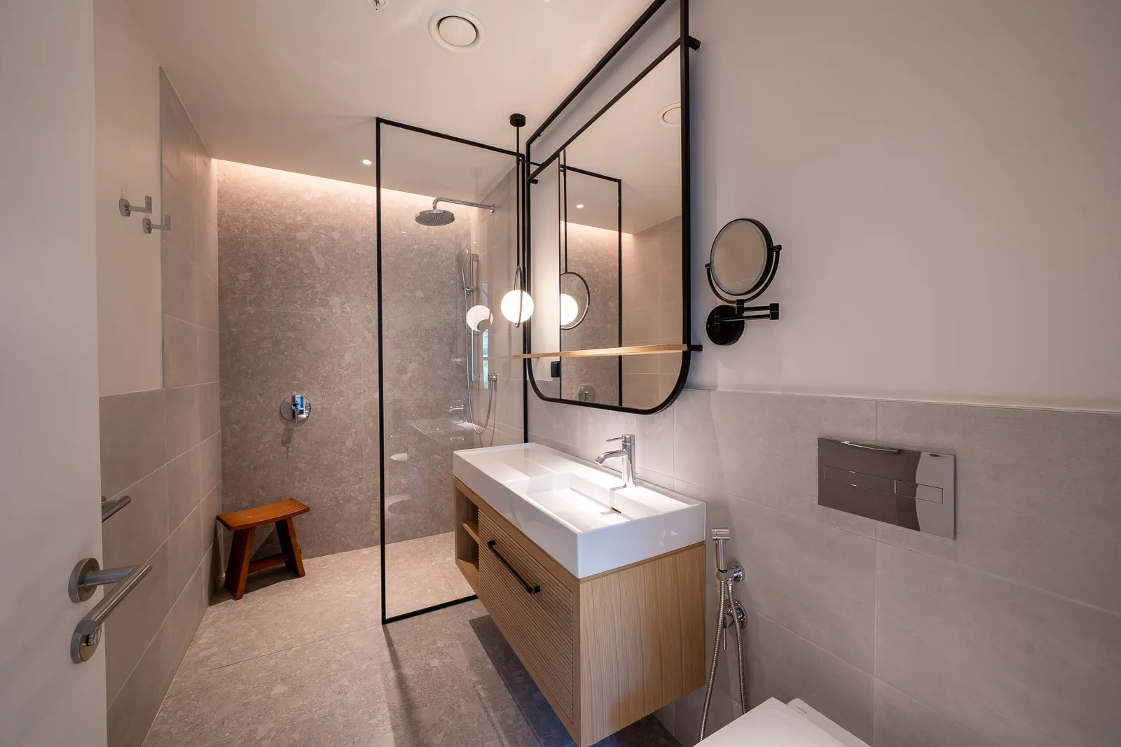 Современная ванная комната с душевой зоной, подвесной раковиной на деревянной тумбе и большим зеркалом в черной раме.