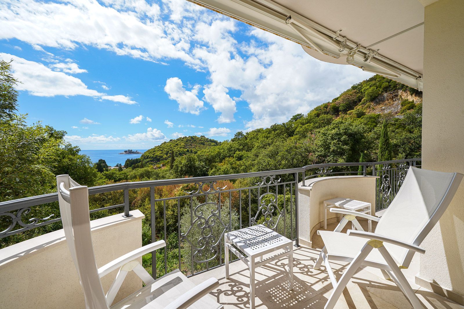 Balkon mit Meer- und Bergblick in einer Wohnung in Petrovac, Montenegro: weiße Möbel, schmiedeeiserne Geländer und Terrasse.