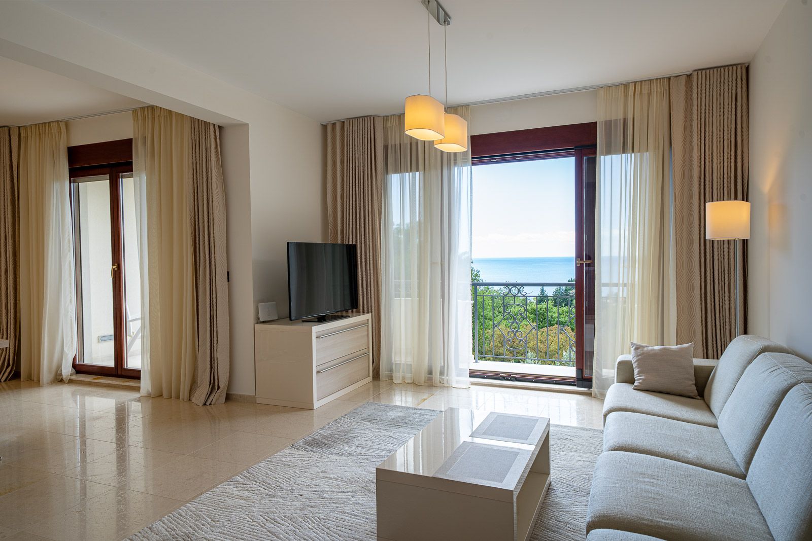 Wohnzimmer in einer Wohnung in Petrovac, Montenegro: helles Interieur, Sofa, TV-Bereich und Panoramablick auf das Meer vom Balkon.