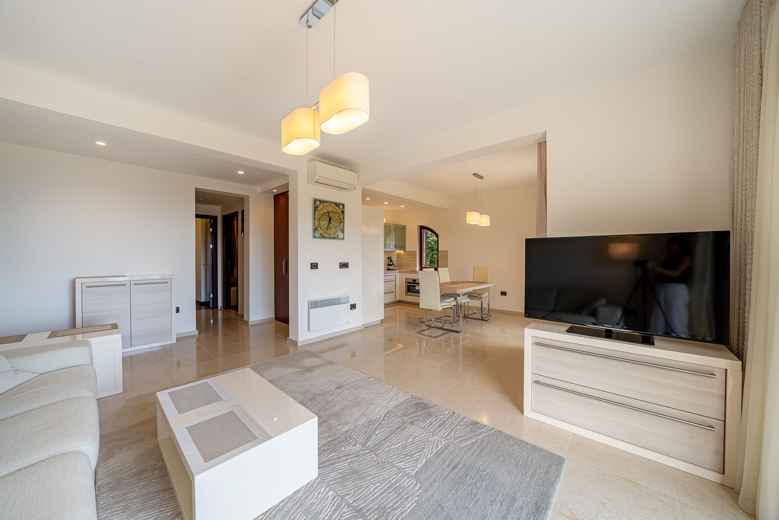 Modernes Wohnzimmer mit Essbereich in einer Wohnung in Petrovac, Montenegro: helle Möbel, TV und Fliesenboden.