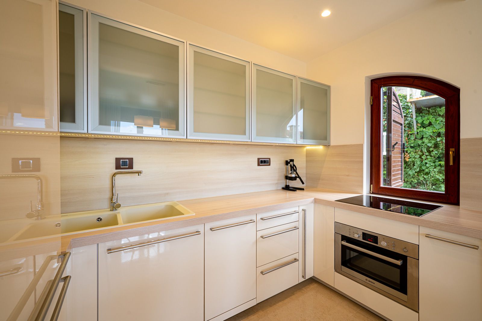Moderne helle Küche in einer Wohnung in Petrovac, Montenegro: Einbaugeräte von Bosch, matte Fronten und Blick in den Garten.