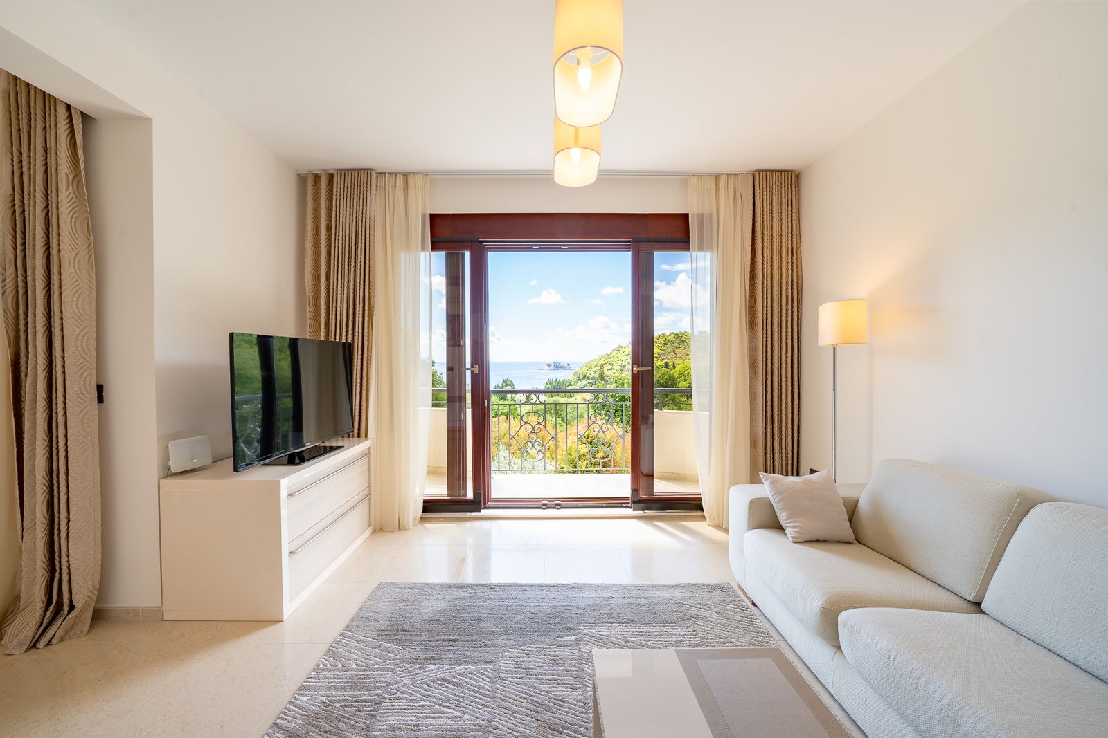 Helles Wohnzimmer in einer Wohnung in Petrovac, Montenegro: moderne Möbel, TV-Bereich und Panoramablick auf das Meer vom Balkon.