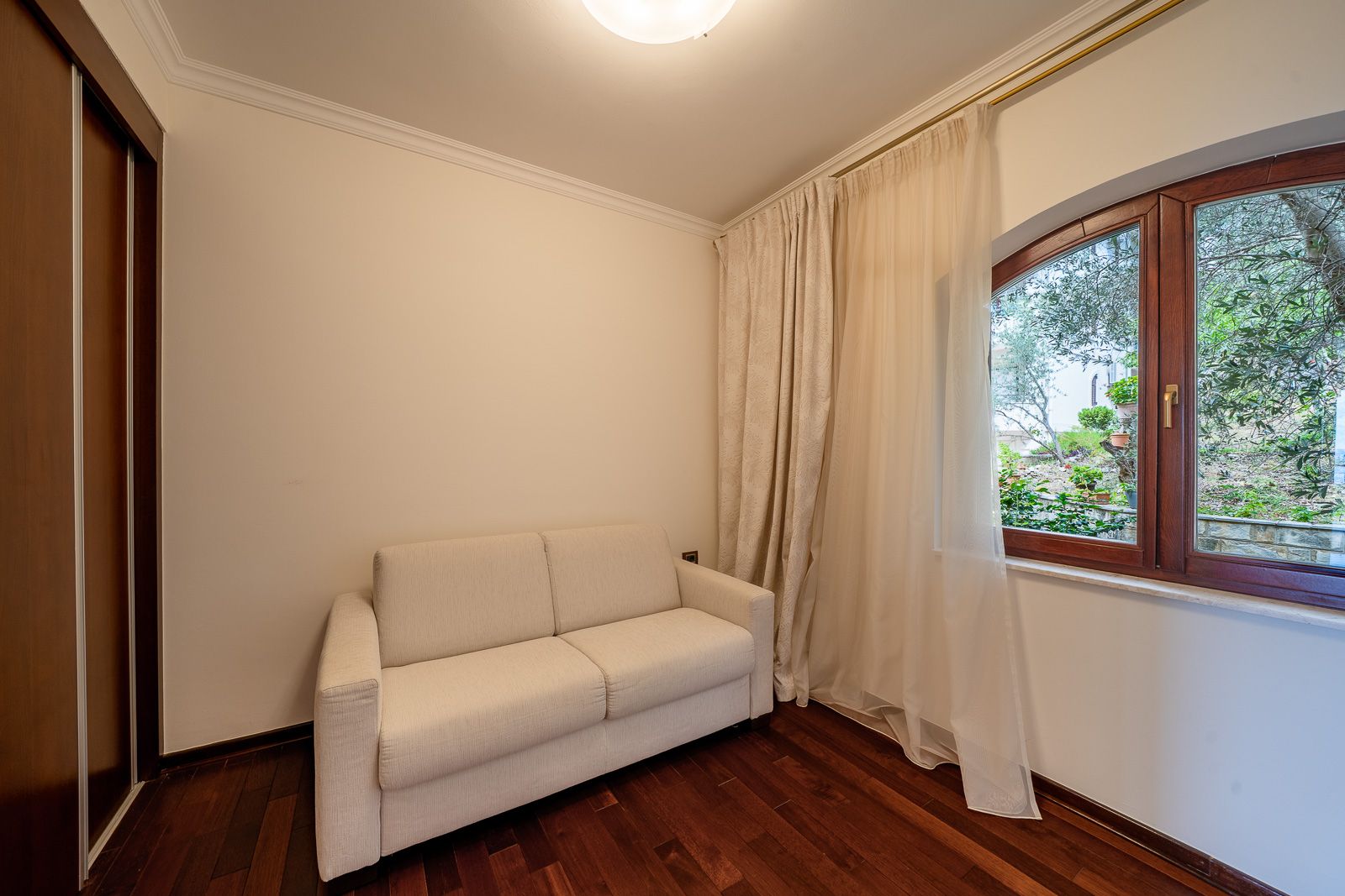 Helles Wohnzimmer mit Sofa und Blick auf den Garten in einer Wohnung in Petrovac, Montenegro: Parkett, Einbauschrank und gemütliches Interieur.