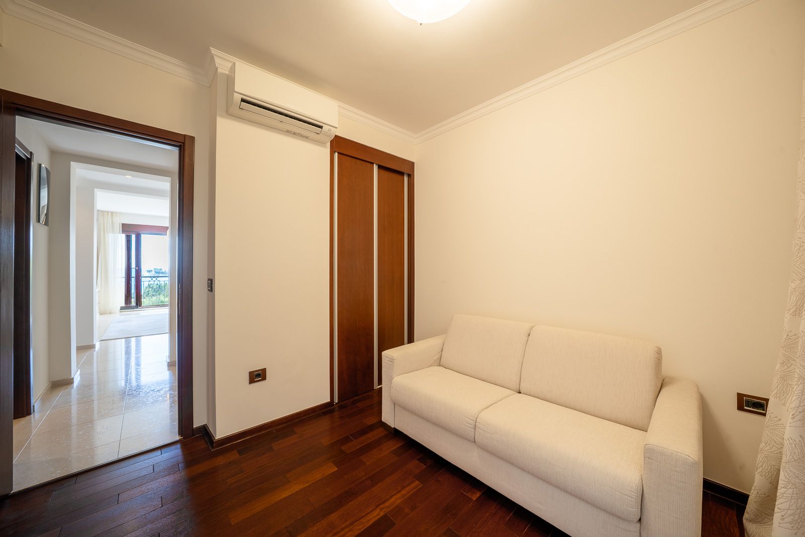 Helles Wohnzimmer mit weißem Sofa und Holzschrank in einer Wohnung in Petrovac, Montenegro, Blick auf die Terrasse.