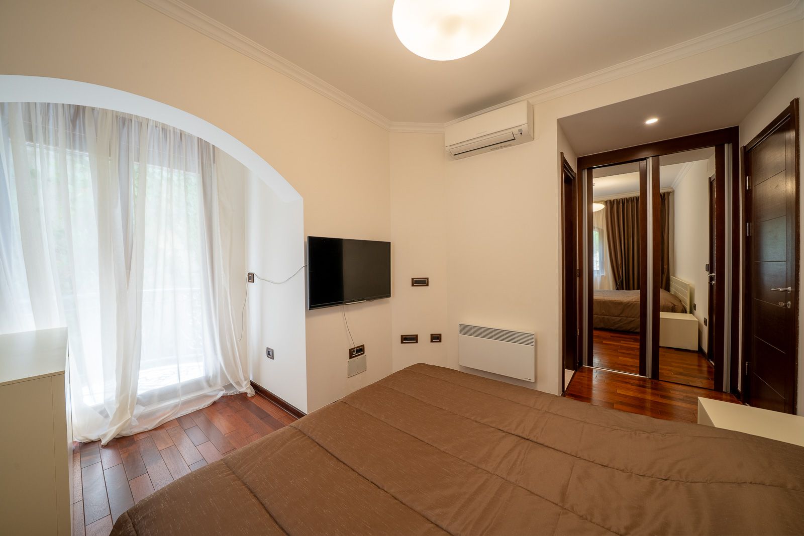 Schlafzimmer in einer Wohnung in Petrovac, Montenegro: Doppelbett, TV, Kleiderschrank mit Spiegel und Parkettboden.